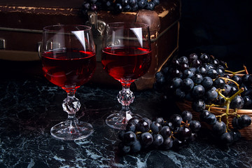 Glass of red wine on dark marble background. Cluster of blue gra