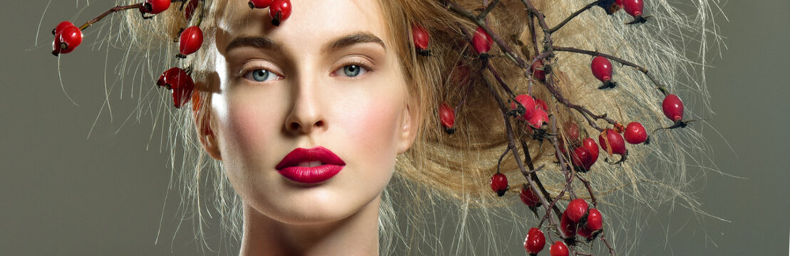 Beautiful woman with a wild rose branches on head. Red berries i