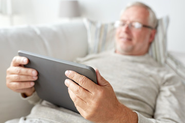 senior man with tablet pc lying on sofa at home