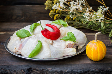 Raw chicken legs on a tray with  red hot pepper and basil. Wooden background. Close-up