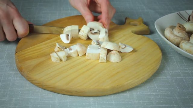 The girl shef in the kitchen sliced mushrooms clean the mushrooms. Cutting on a wooden board.
