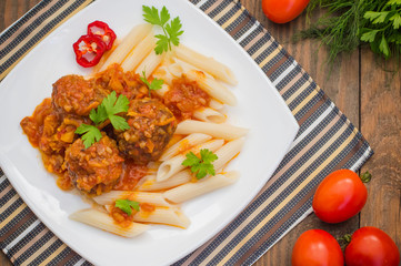Meatballs with pasta penne in tomato sauce on a white plate. Wooden rustic background. Top view. Close-up