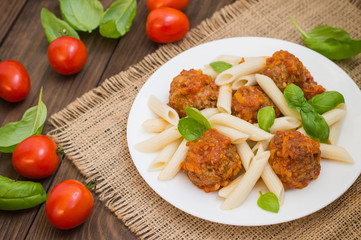 Meatballs with pasta penne in tomato sauce on a white plate. Wooden rustic background. Top view. Close-up