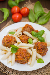 Meatballs with pasta penne in tomato sauce on a white plate. Wooden rustic background. Top view. Close-up