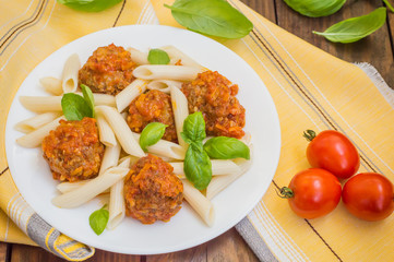 Meatballs with pasta penne in tomato sauce on a white plate. Wooden rustic background. Top view. Close-up
