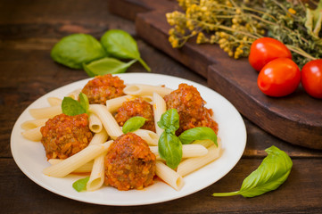 Meatballs with pasta penne in tomato sauce on a white plate. Wooden rustic background. Top view. Close-up