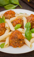 Meatballs with pasta penne in tomato sauce on a white plate. Wooden rustic background. Top view. Close-up