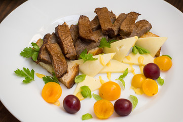 Sliced roast beef on toast, cheese, basil, berries, plum and Dutch sauce. Restaurant supply  a wooden background. Top view. Close-up