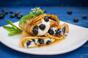 Pancakes with blueberries, whipped cream and a sprig of mint  lemon balm. Wooden blue background. Close-up.