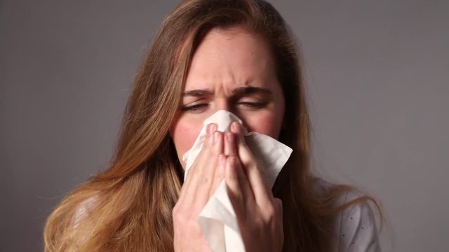sick young woman sneezing, blowing her nose with a tissue