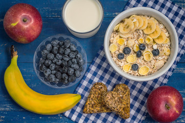 Useful and very tasty breakfast, oatmeal flakes, blueberries, bananas, milk, peaches  kozinaki, Georgian sweets. Wooden blue background. Top view. Close-up