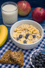 Useful and very tasty breakfast, oatmeal flakes, blueberries, bananas, milk, peaches  kozinaki, Georgian sweets. Wooden blue background. Top view. Close-up