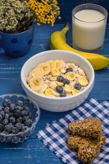 Useful and very tasty breakfast, oatmeal flakes, blueberries, bananas, milk, peaches  kozinaki, Georgian sweets. Wooden blue background. Top view. Close-up