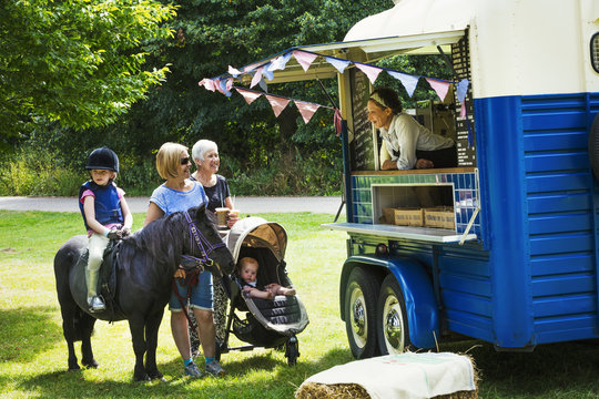 People and girl on pony queueing at a blue mobile coffee shop.