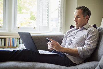A man seated on a sofa at home using a laptop.