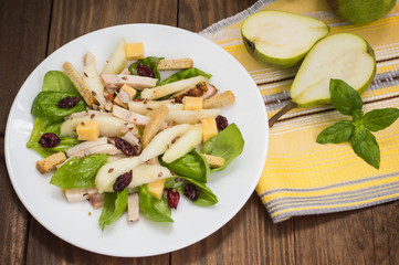 Chicken salad, pears, dried gooseberries and currants, cheese on basil leaves. Wooden background. Top view. Close-up