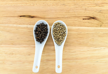 Close up black and white pepper in white ceramic spoon on block wooden