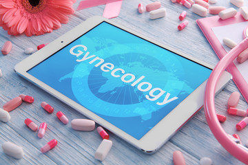 Tablet with word GYNECOLOGY and pills on wooden background