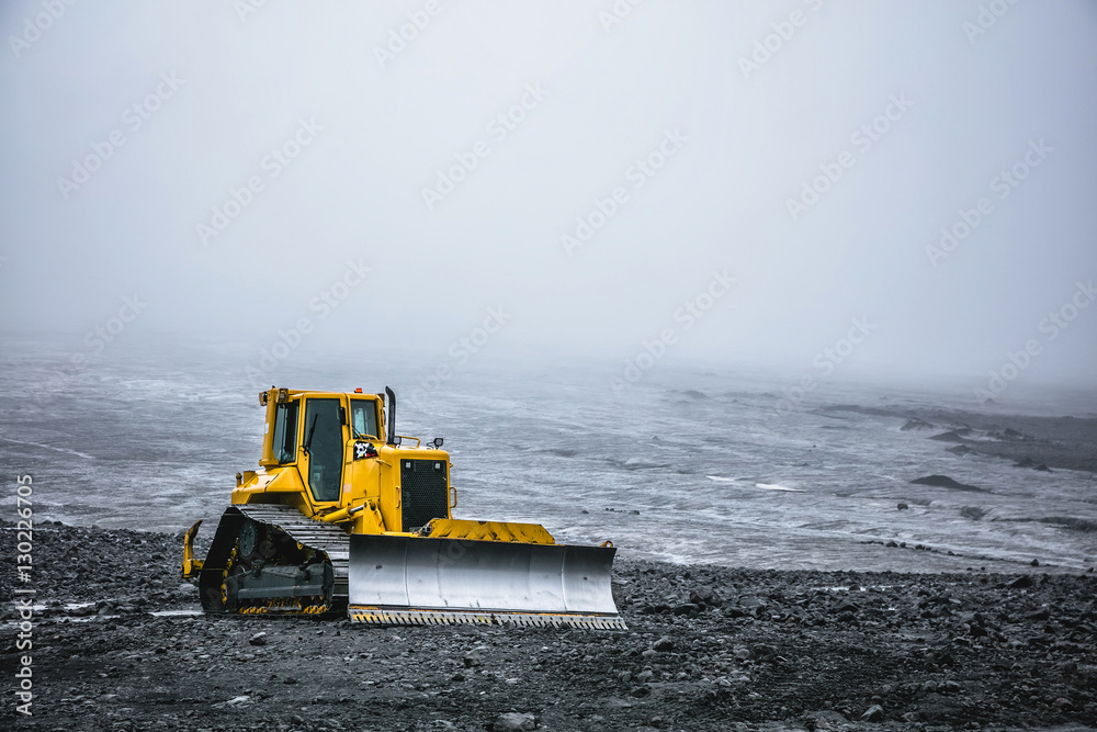 Wall mural Bright yellow bulldozer on a background of gray desert plateau. Summer in 2016 Iceland