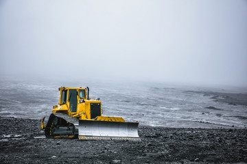 Bright yellow bulldozer on a background of gray desert plateau. Summer in 2016 Iceland - obrazy, fototapety, plakaty