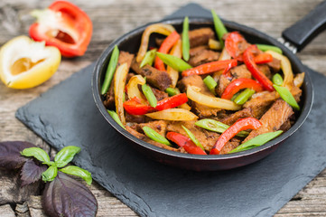 Sauteed beef with vegetables in a pan. Wooden background. Top view. Close-up