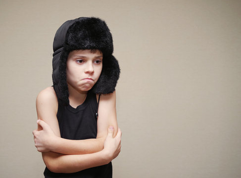Boy in a cap with ear-flaps and a gymnastic undershirt on a light background. Conceptual image of the frozen person