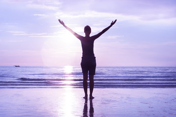 Fototapeta premium Open mindedness and happiness concept. Woman's silhouette on sunset beach. Stretched out hands to the sky.