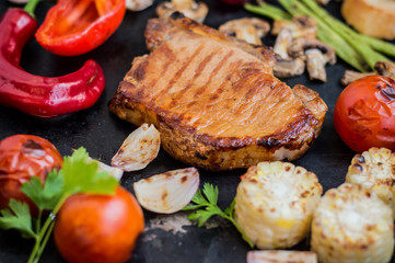 Steak on the bone with vegetables cooked  the grill. Black stone background. Top view. Selective focus close-up