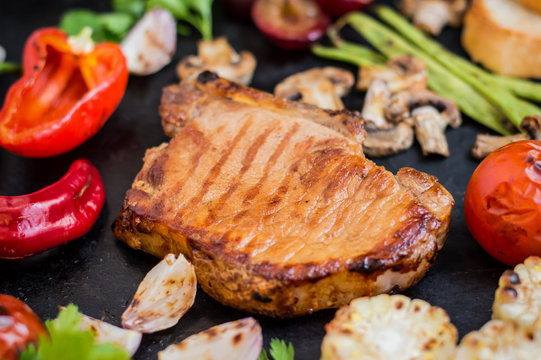 Steak on the bone with vegetables cooked  the grill. Black stone background. Top view. Selective focus close-up