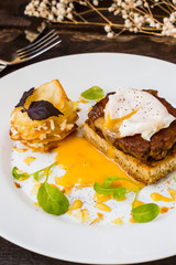 Dish with meat steak on toast, potato chips  melted cheese and poached egg  Dutch sauce. Wooden background. Top view. Close-up