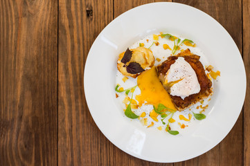 Dish with meat steak on toast, potato chips  melted cheese and poached egg  Dutch sauce. Wooden background. Top view. Close-up