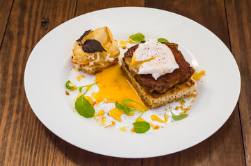 Dish with meat steak on toast, potato chips  melted cheese and poached egg  Dutch sauce. Wooden background. Top view. Close-up
