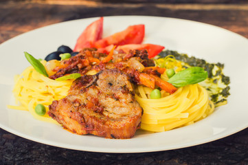 Tagliolini with meat in tomato sauce, olives and   spinach. Wooden background. Close-up. Top view
