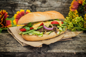 Sandwich with veal steak, greens, zucchini, tomatoes, cheese and mustard sauce. Wooden background. Close-up. Selective focus