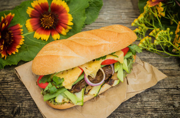 Sandwich with veal steak, greens, zucchini, tomatoes, cheese and mustard sauce. Wooden background. Close-up. Selective focus