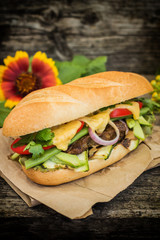 Sandwich with veal steak, greens, zucchini, tomatoes, cheese and mustard sauce. Wooden background. Close-up. Selective focus