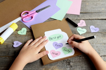 Kid doing a greeting card. Kid holds a black marker in hand and writes wishes. Paper greeting card...