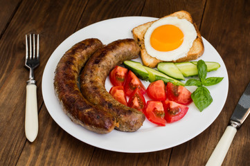 Nutritious breakfast consisting of fried sausage,  eggs, toast, fresh cucumbers and tomatoes. Wooden rustic background. Top view. Close-up