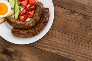 Nutritious breakfast consisting of fried sausage,  eggs, toast, fresh cucumbers and tomatoes. Wooden rustic background. Top view. Close-up
