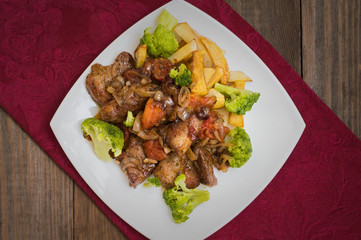 Stifado - a traditional Cypriot dishes, spread in Greece. It consists of  stew with tomatoes, potatoes, broccoli, onions, garlic and spicy spices. Wooden rustic table. Top view. Close-up