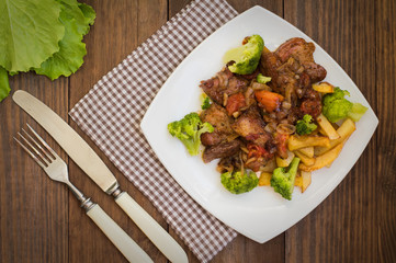 Stifado - a traditional Cypriot dishes, spread in Greece. It consists of  stew with tomatoes, potatoes, broccoli, onions, garlic and spicy spices. Wooden rustic table. Top view. Close-up