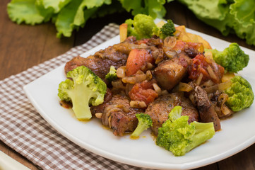 Stifado - a traditional Cypriot dishes, spread in Greece. It consists of  stew with tomatoes, potatoes, broccoli, onions, garlic and spicy spices. Wooden rustic table. Top view. Close-up