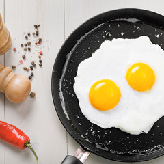Two fried eggs in a frying pan cooked for breakfast. Delicious international meal on a table. Homemade food, top view.