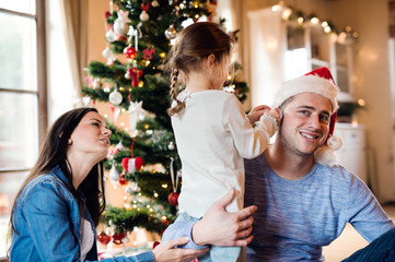 Young family with daugter at Christmas tree at home.