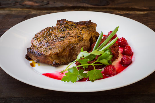 Fried Grilled pork steak on the bone with vegetables, mashed beetroot and berry sauce. Wooden background. Top view. Close-up
