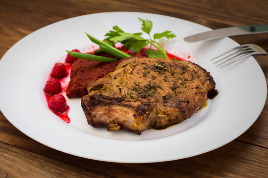 Fried Grilled pork steak on the bone with vegetables, mashed beetroot and berry sauce. Wooden background. Top view. Close-up