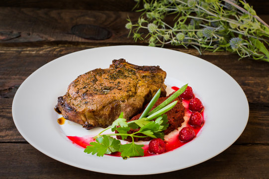 Fried Grilled pork steak on the bone with vegetables, mashed beetroot and berry sauce. Wooden background. Top view. Close-up