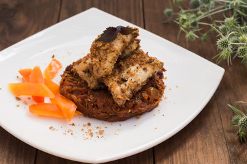 Fish coated in crumbs on vegetable cushion with squash, tomatoes, carrots and onions. Wooden rustic background. Close-up
