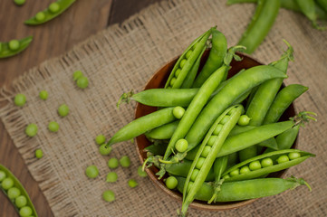 Pea pods in a wooden bowl on sacking.  background. Top view. Close-up