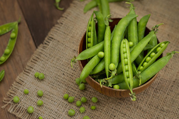 Pea pods in a wooden bowl on sacking.  background. Top view. Close-up